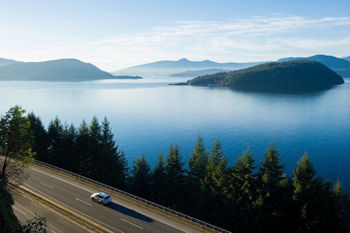 A car driving down the road next to trees and a lake