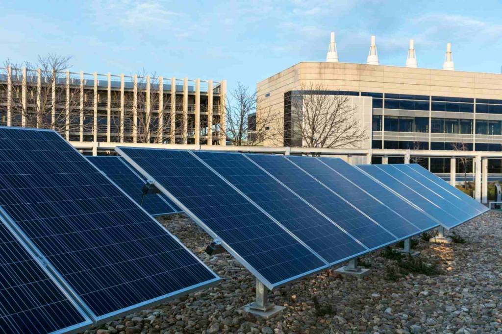 Image of a solar panel with a wind turbine in the background