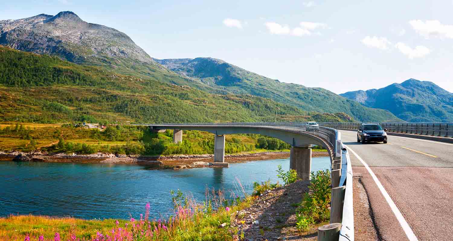 Cars crossing a bridge over a river with mountains in the background