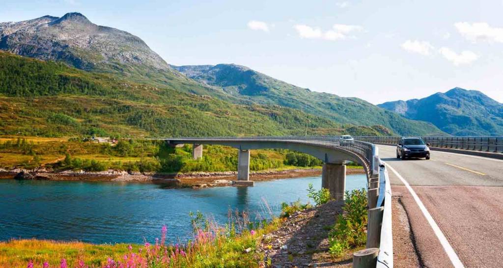 Un coche circulando por una carretera rodeada por un río y montañas