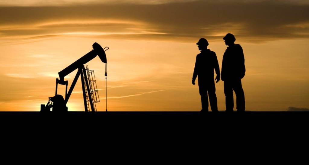 Two men looking at a pump jack at dusk 