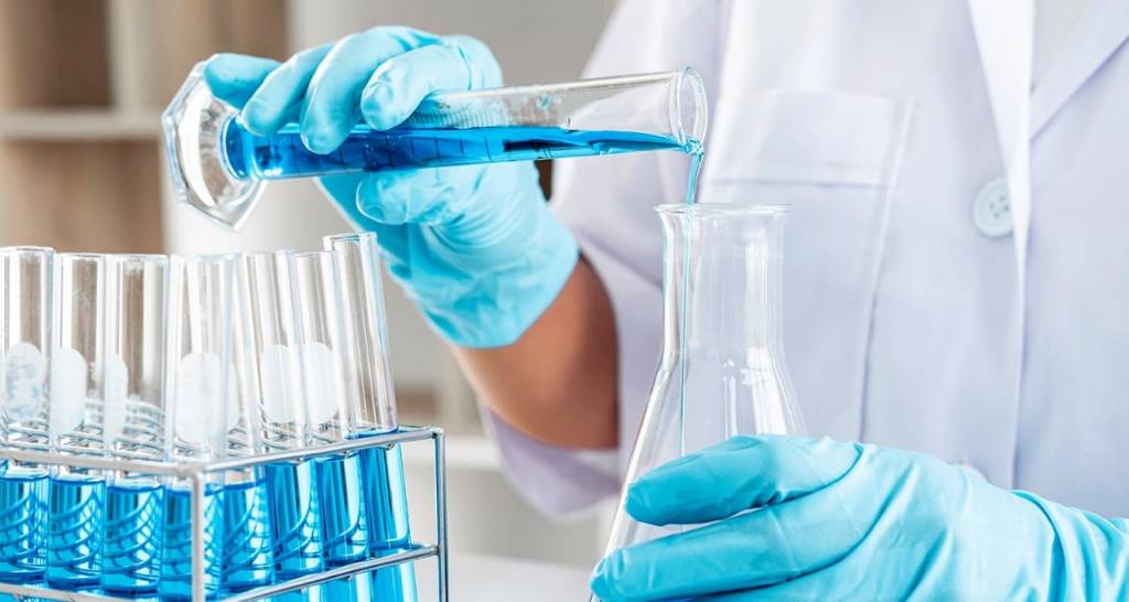 View of a scientist&apos;s hands while handling two containers of liquid.