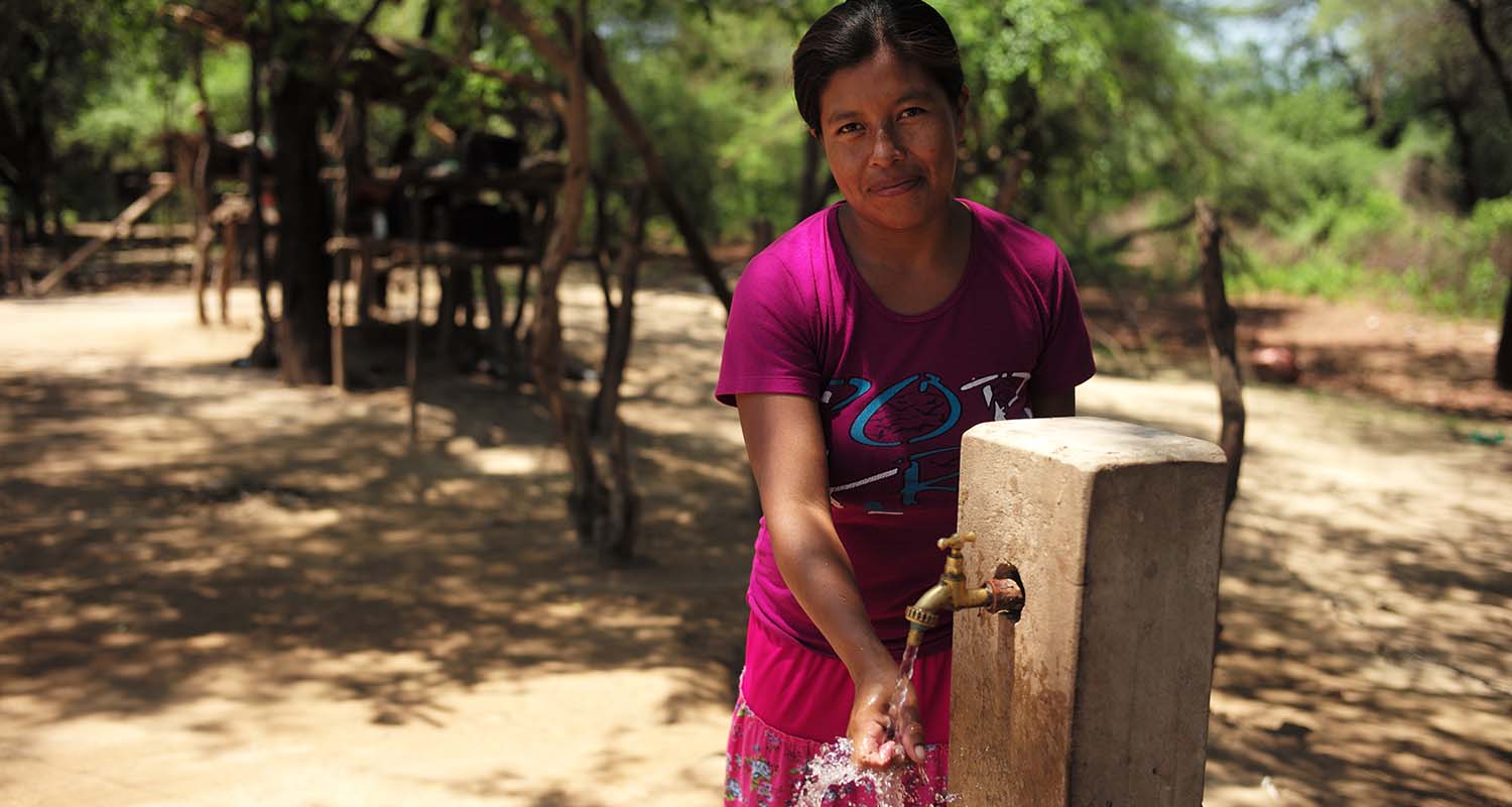 Bolivian woman running water over hand at fountain